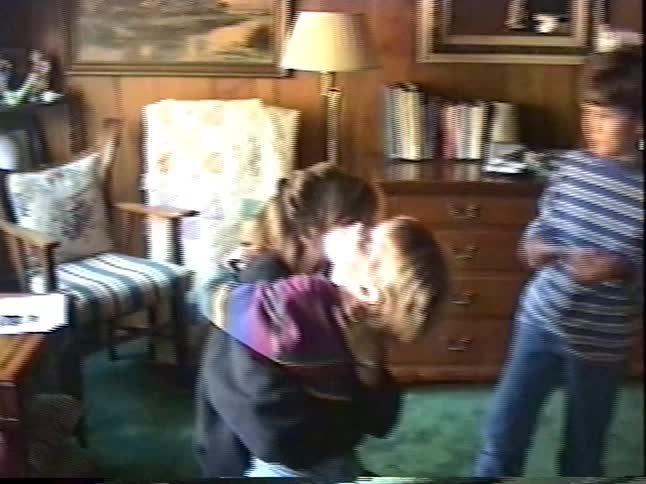 A young boy kisses his mom, and his siblings join in for a big group hug in a cozy, vintage living room