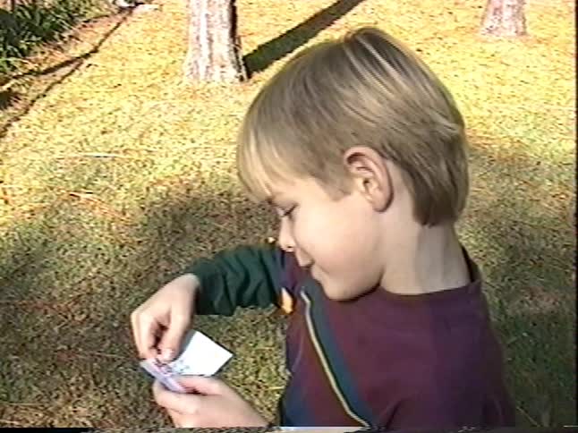 Vintage VHS footage shows two young boys playing with a paper fortune teller in their backyard before running off into the woods