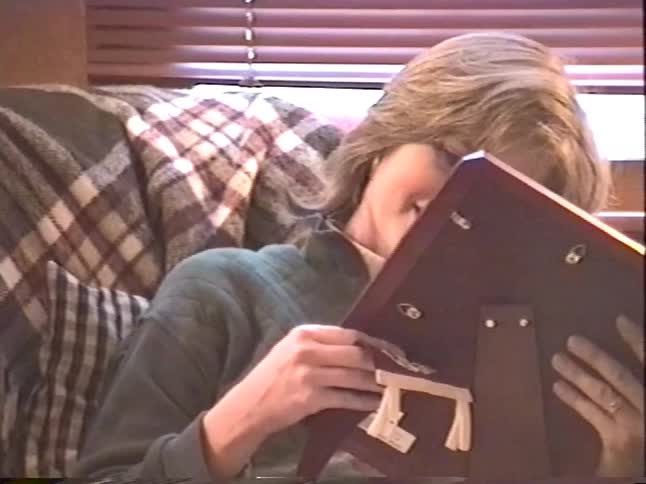 A happy woman opens a picture frame for a gift while sitting in a cozy armchair surrounded by presents