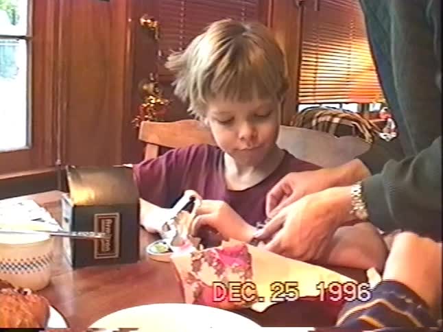 A young boy excitedly unwraps a brand new wristwatch for Christmas as his mother helps him put it on in a classic 1990s home video