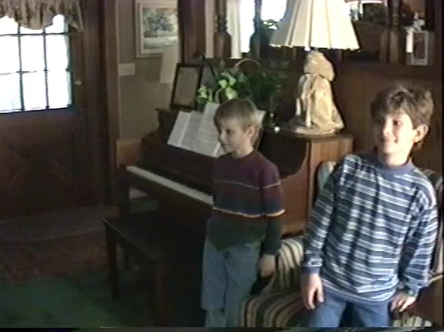Two curious young boys play around a piano in their living room in a nostalgic 1990s home video