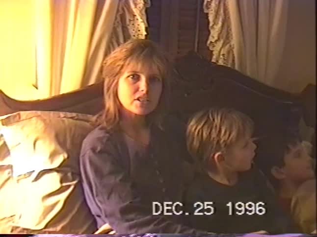 A mother and her two young sons sit together on a bed on Christmas night in this intimate VHS home video from 1996