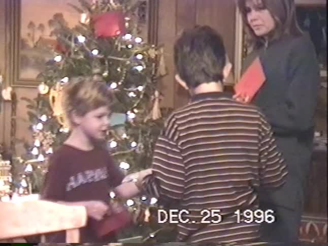 Vintage 1996 home video shows a mother and her two sons opening Christmas cards together in a cozy living room next to the tree