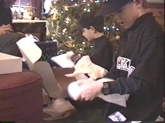 A mother helps her two young sons unwrap presents on Christmas morning in front of their decorated tree