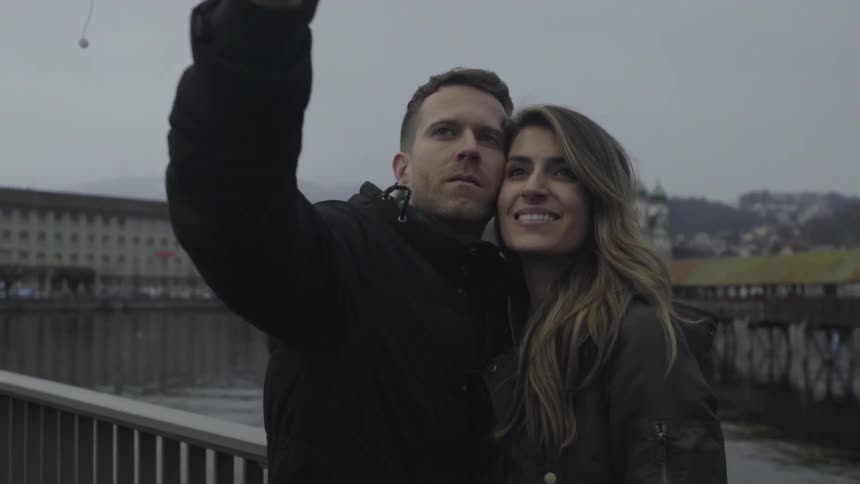 A man and woman take a selfie on a bridge overlooking a river