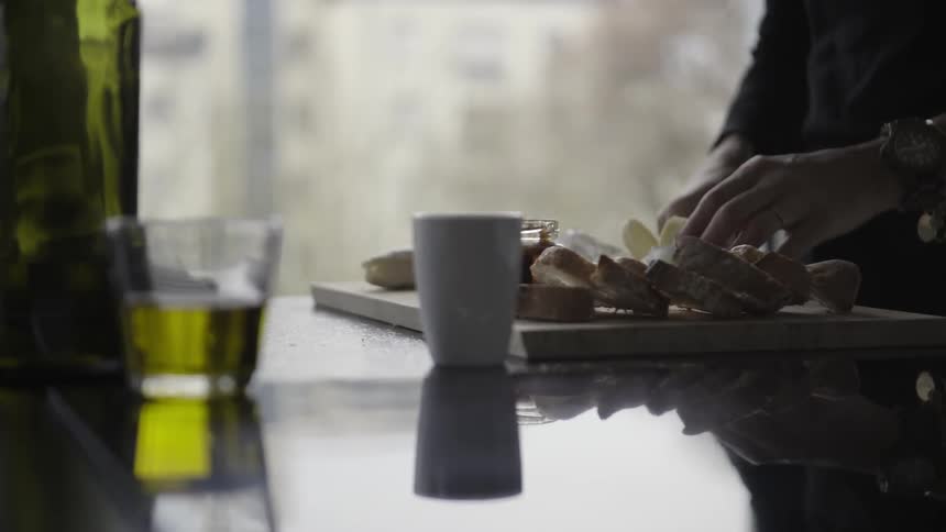 A woman is slicing cheese to place on a board with bread