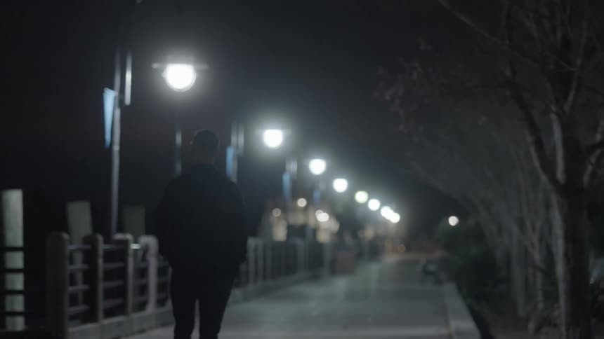 Man walking down a sidewalk at night lit by street lights