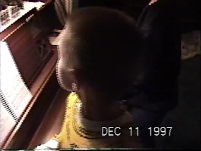 Vintage 1997 VHS footage shows a young boy admiring a miniature Christmas village on a piano