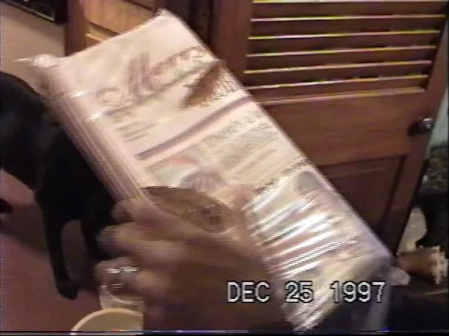 A vintage VHS clip from Christmas 1997 shows a special edition newspaper while a black dog drinks from a bowl in the background