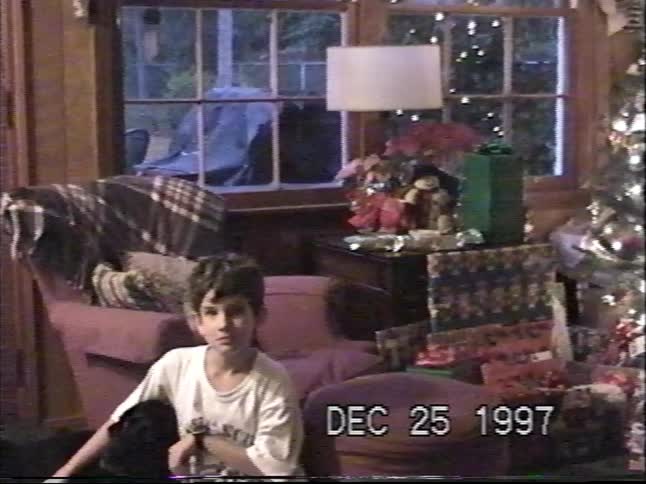 A young boy sits with his black dog on the floor of a cozy living room on Christmas morning in 1997