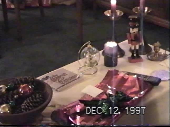 Vintage 1997 home video footage of a tabletop decorated for Christmas with a nutcracker, lit candles, ornaments, and a gift