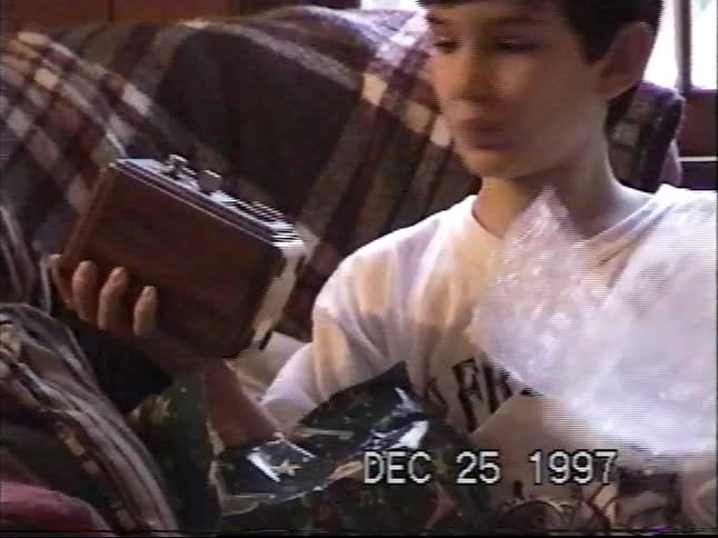 A young boy examines a vintage-style wooden clock radio he received for Christmas in 1997