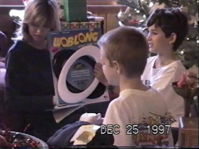 A woman and two young boys open presents together on Christmas morning in a home video from 1997