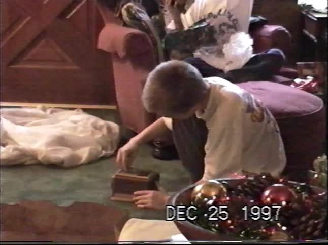 Vintage VHS footage shows a young boy excitedly opening a wooden box on Christmas morning in 1997