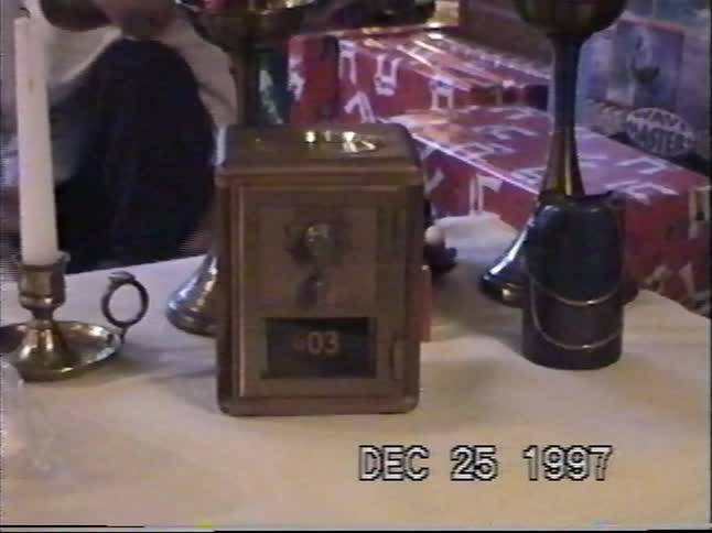 A vintage brass post office box bank sits on a table surrounded by Christmas presents and decorations in 1997