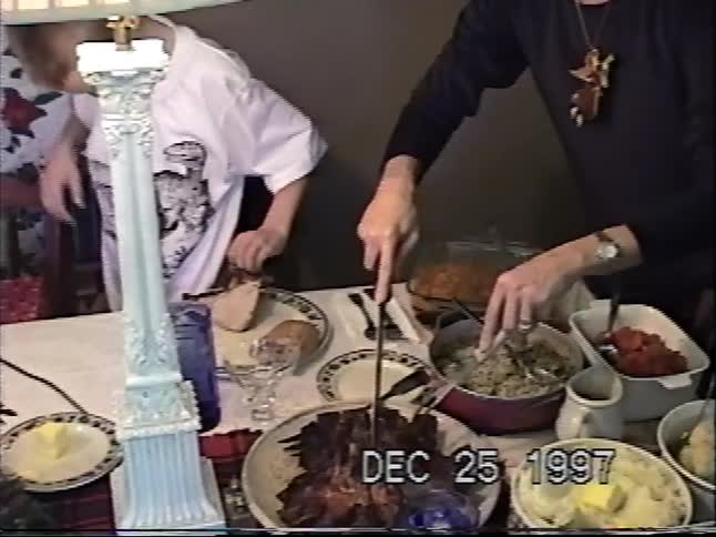 A woman carves the main course at a family Christmas dinner table full of delicious food in this vintage 1997 home video