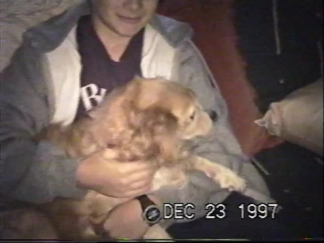 A young boy holds his cute, fluffy dog while sitting on a couch in an authentic home video from 1997