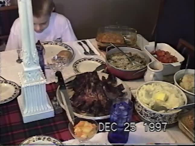 A young boy makes a funny face at the camera while sitting at the table for Christmas dinner in this vintage 1997 home video