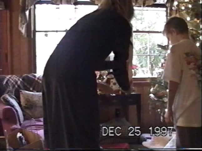 Vintage VHS footage from 1997 shows siblings opening presents on Christmas morning next to a decorated tree