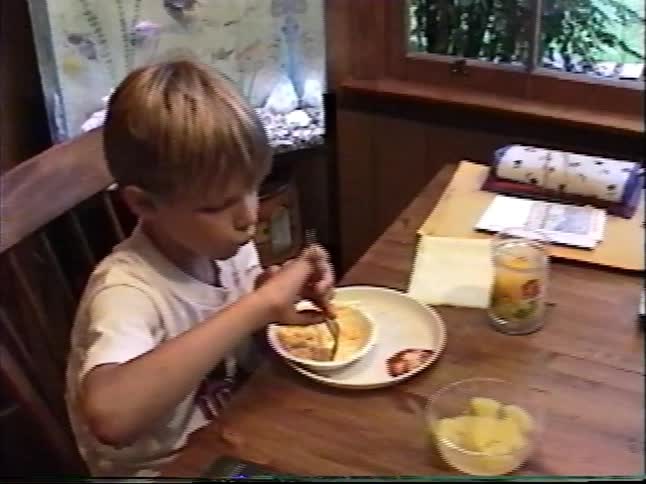 Young boy eating breakfast alone at a wooden kitchen table in a cozy home dining room