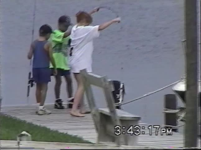 Vintage home video footage shows a woman and two young boys fishing off a dock and catching a fish