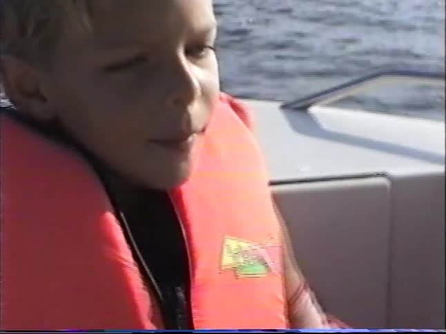 Vintage footage of two young boys wearing life vests on a boat ride past a distant lighthouse