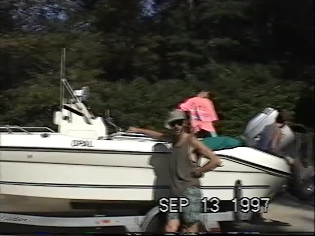Three friends pose with their motorboat before a day on the water in this 1997 home video