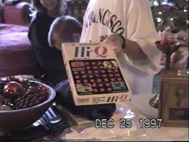 A boy holds up his new Hi-Q board game while his younger brother opens presents on Christmas morning 1997