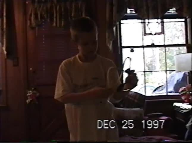 A young boy excitedly unboxes and plays with his new slingshot on Christmas morning in 1997