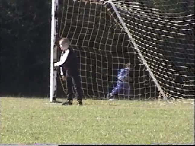 Vintage VHS footage shows a young boy sadly leaning against a soccer goal post during a game