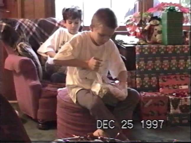 Two young boys excitedly open their stocking stuffers on Christmas morning in a cozy living room in 1997