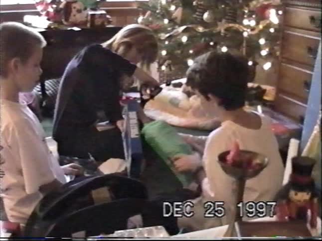 Vintage VHS footage from 1997 shows a family with two young boys opening gifts on Christmas morning by the tree