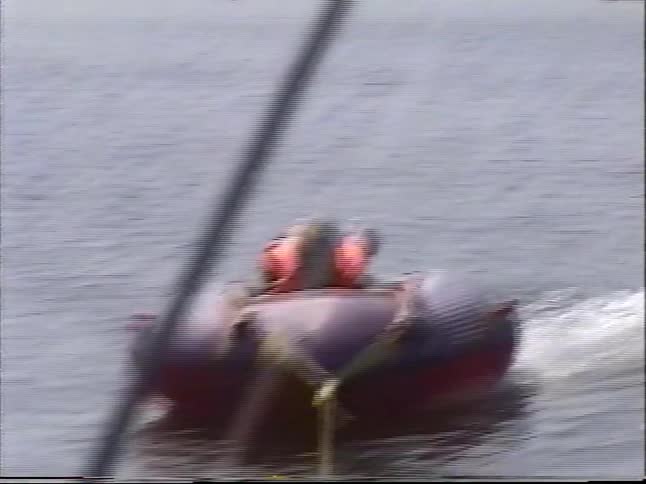 A young girl wearing a life vest enjoys being pulled on an inflatable tube by a boat on a sunny lake day