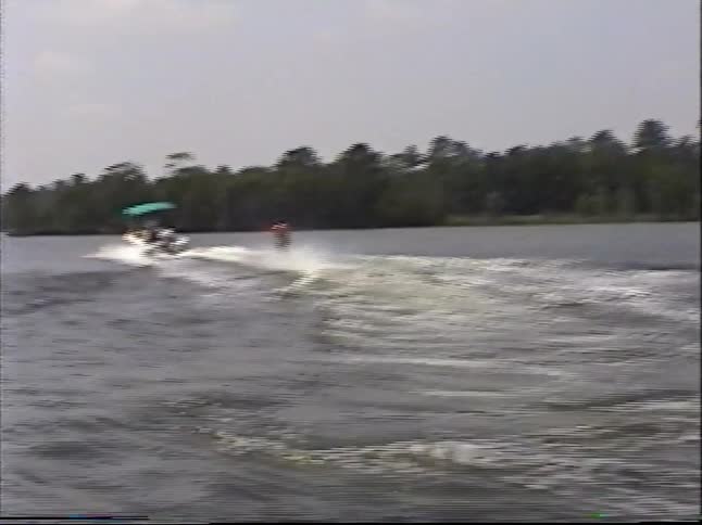 A man in a life vest enjoys a day of water skiing as he's pulled by a motorboat across a calm lake