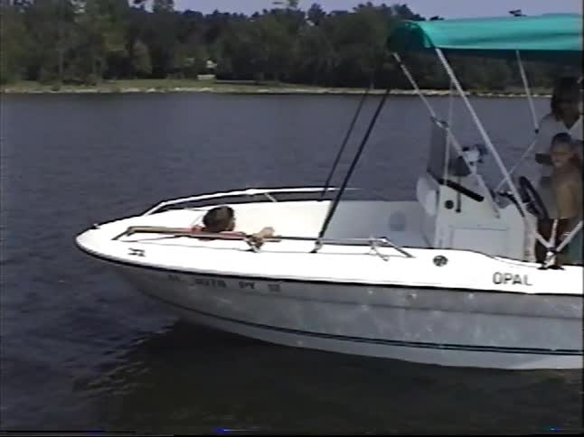 A family with children enjoys a sunny day boating on a lake as a boy climbs aboard to put on his life vest