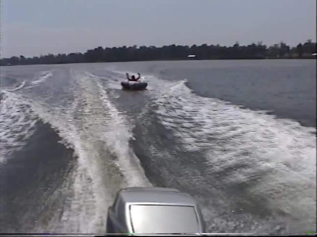 Vintage VHS footage captures the fun of riding an inflatable tube behind a speedboat on a wide river