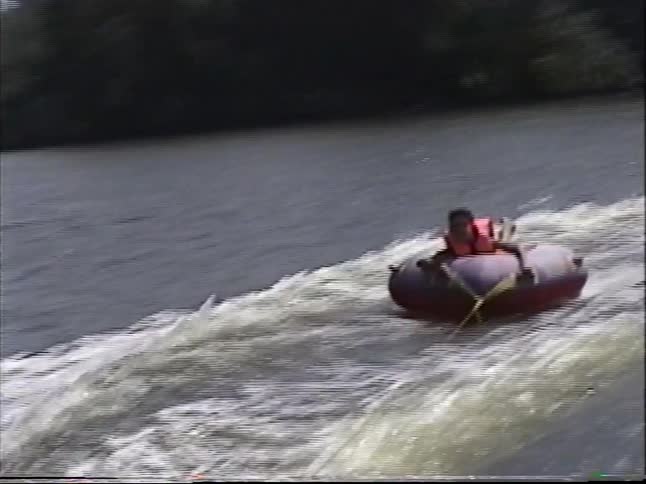 A young person has a blast tubing behind a speedboat on a sunny day in this vintage home video footage