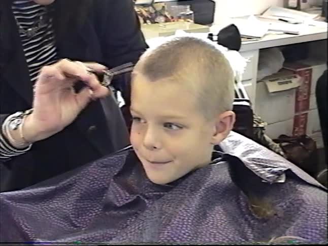 Vintage home video footage shows a cute young boy happily getting his hair cut by a stylist at a salon