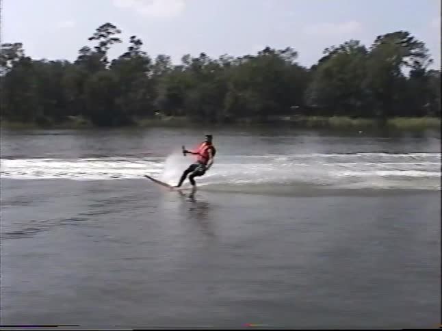 Vintage 1990s home video footage shows a man water skiing and then slalom skiing across a calm river