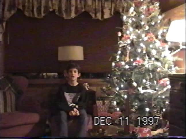A nostalgic 1997 home video shows a young boy talking to the camera while sitting by a lit Christmas tree