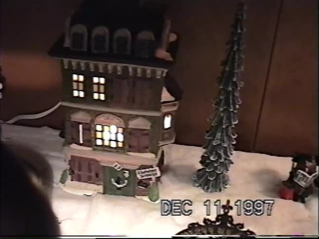 Vintage 1997 home video footage slowly pans across a detailed miniature Dickens' Village Christmas display with lit houses and fake snow