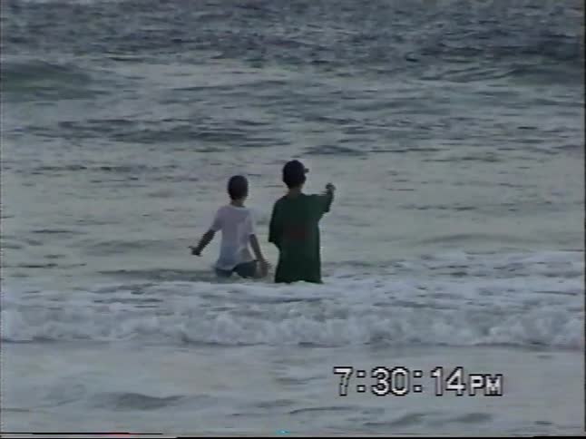 Vintage home video captures two young boys joyfully splashing and playing in the ocean surf