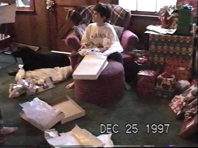 Two young boys open presents on Christmas morning in 1997 while their dog watches