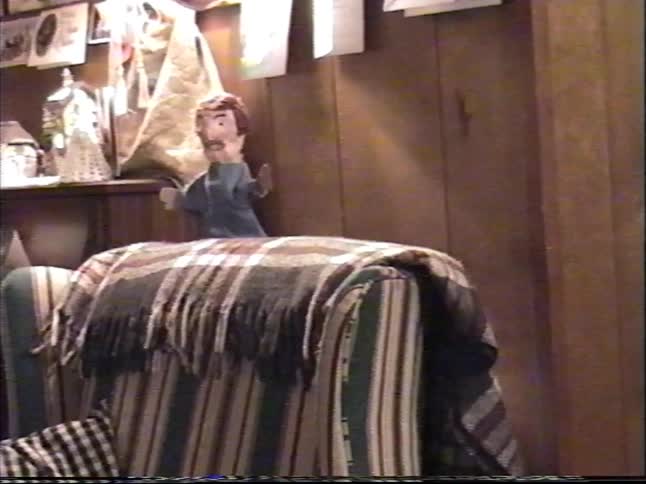 A low-angle VHS home video of a puppet show in a cozy living room, ending with a little boy playfully grabbing the puppet