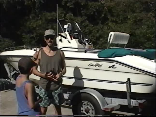 Vintage VHS footage shows a father and his son proudly posing in front of their new motorboat