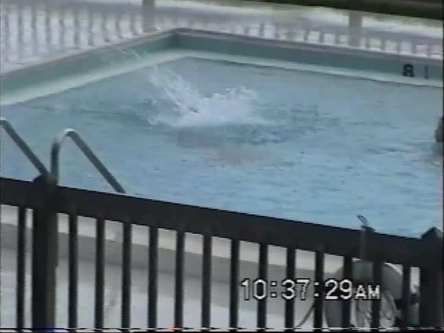 Vintage VHS footage from a balcony shows two boys swimming and playing in a pool by a marina on an overcast day