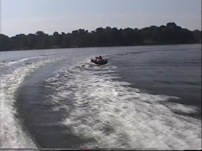 A vintage VHS home movie captures the fun of being pulled on an inflatable tube by a motorboat across a wide river
