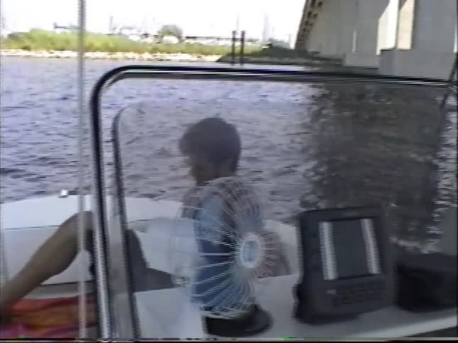 Home movie footage from the 1990s shows a relaxing boat trip passing by a marina and underneath a large concrete bridge