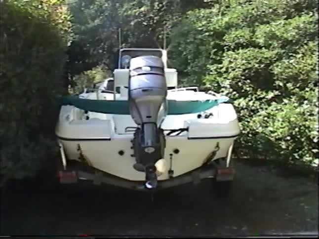 A motorboat on a trailer is carefully backed down a long, wooded driveway for storage