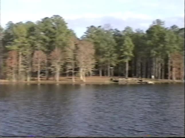 A vintage home video shows a young boy on a dock, followed by a pan across a calm lake to a family canoeing